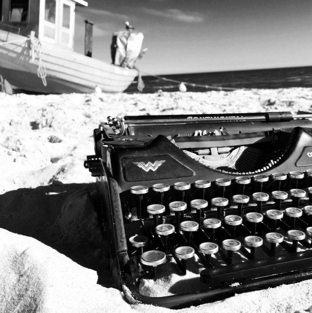 Alte Schreibmaschine Continental auf dem Strandsand. Im Hintergrund ein altes Fischerboot.